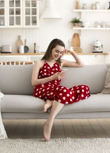 Smiling young girl sit on sofa text message on phone