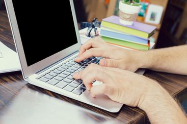 Person typing on a laptop with books and a plant in a...