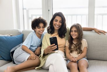Two joyful little kids and mom using smartphone at home