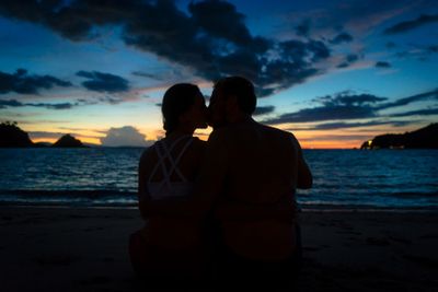 Young couple kissing on a dreamy beach at dusk during...