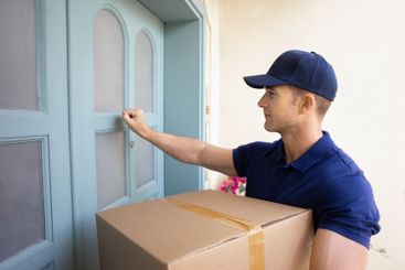 Male courier in uniform cap knocking on customers door