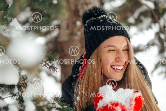 Happy smiling young woman having fun with snow in a...