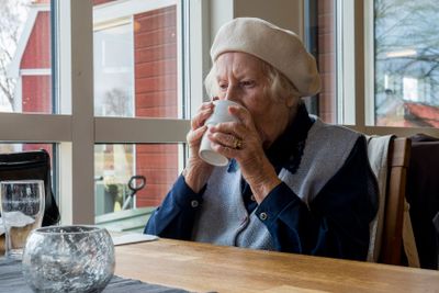 Äldre kvinna dricker kaffe efter maten.
