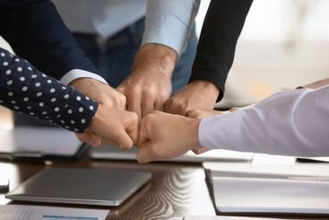 Team fists bumping gathered together at conference table