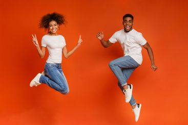 Excited black couple jumping on orange background