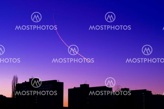 Airplane condensation trail over the silhouettes of...