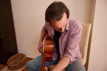 Man tuning an acoustic guitar while seated indoors...