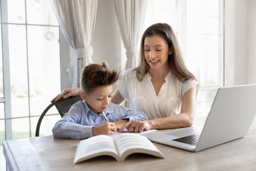 Happy mom helping schoolkid son with school homework