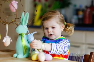Cute little toddler girl decorating tree and bunny with...