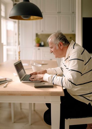 Side view of retired senior man using laptop at dining...