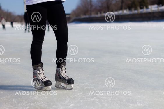 A pair of legs with ice skates on the ice during winter