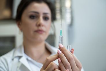 A focused nurse in a white lab coat carefully prepares a...