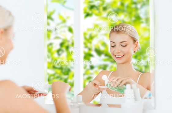 young woman with lotion washing face at bathroom