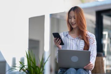 Woman is sitting on a chair and using a laptop and a...
