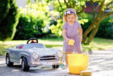 Cute gorgeous toddler girl washing big old toy car in...