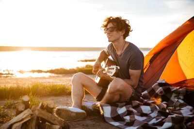 Smiling man sitting near touristic tent and playing guitar