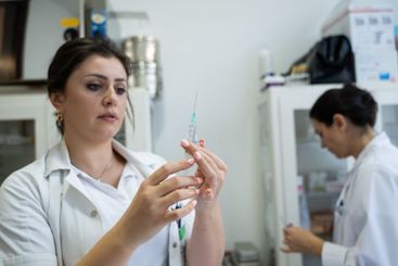 A focused nurse in a white lab coat carefully prepares a...