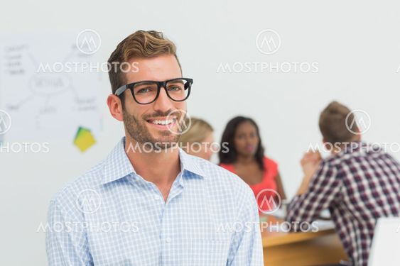 Handsome designer smiling at camera with colleagues behind him