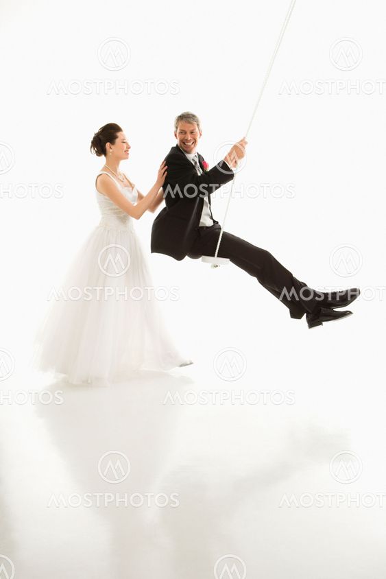Bride pushing groom in swing.