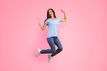 Happy lady jumping over yellow studio wall