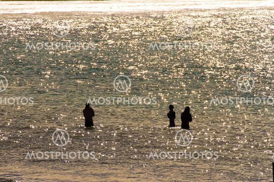 Three men stand in ocean bay with sun reflection