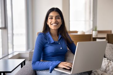 Happy woman smiling, using laptop seated on sofa