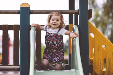 Cute toddler girl playing on slide on outdoor...