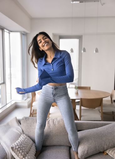 Happy Indian woman dancing jumping on sofa at home