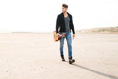 Portrait of a casual man walking across seashore with...