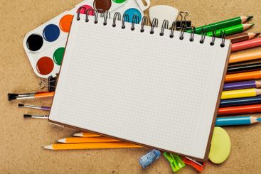 Blank sketchbook surrounded by colorful art supplies on...