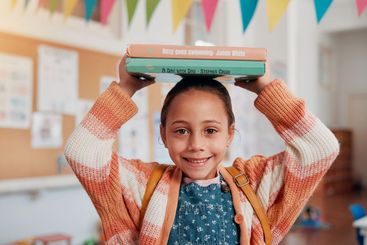 Girl, smile and books on head in classroom, portrait and...