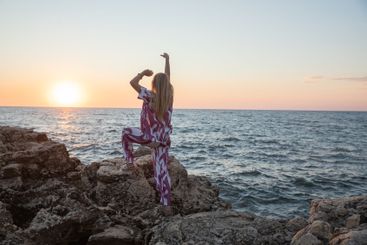 blonde woman on a rock by the sea at sunset hands up