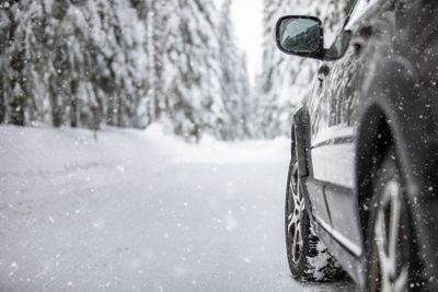 Car on a snowy winter road amid forests - using its four...