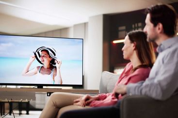 Man and woman relax on sofa, watching TV