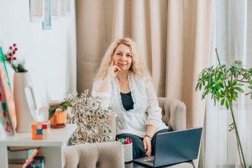 woman with laptop in cozy home office on beige armchair,...