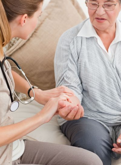 Beautiful nurse taking the pulse of her patient at home