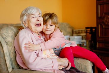 Beautiful toddler girl and great-grandmother hugging...