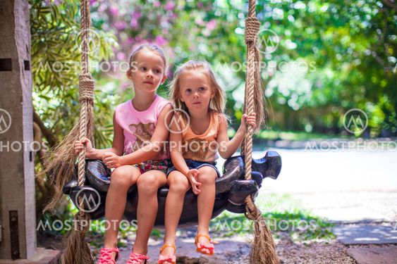 Little girls swinging in a cozy lovely flowered courtyard