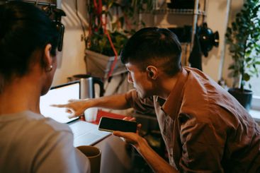 Male freelancer holding smart phone and explaining female...