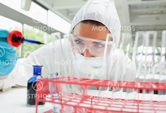 Protected female science student dropping blue liquid in a test