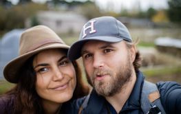 Happy young married couple smiling with a farmyard behind...