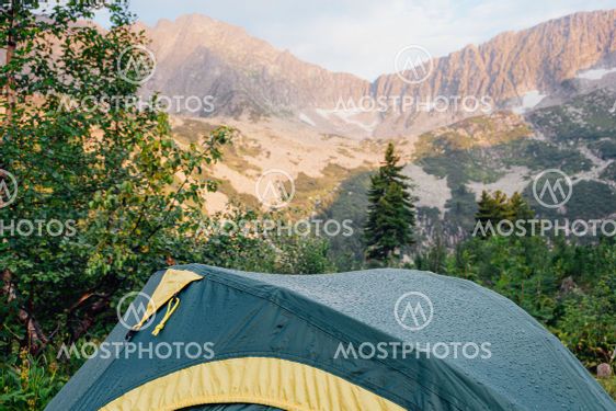 Green tent in forest at foot of mountain range. Hiking...