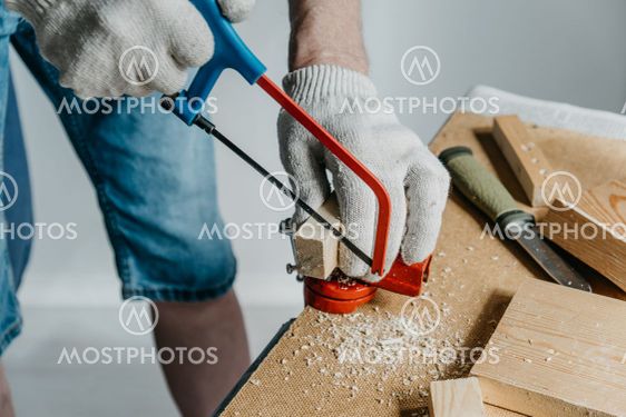 A man in work gloves is sawing a small block of wood...
