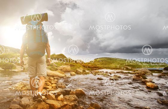 Hiker man with backpack crossing a river.