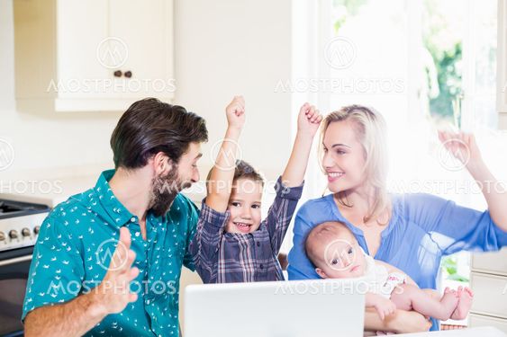 Excited parents and kids using laptop in kitchen