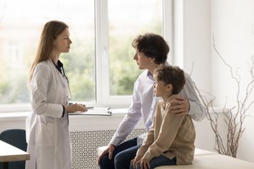 Father sitting on couch with little son listen to doctor