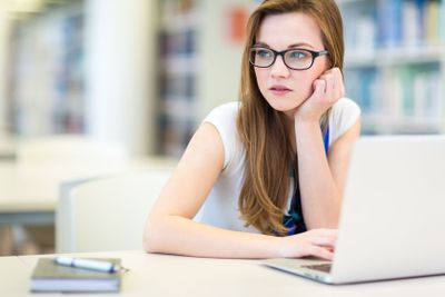 Pretty, female college student in a library, looking for...