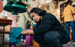 Female entrepreneur cleaning merchandise with rag while crouching at antique store