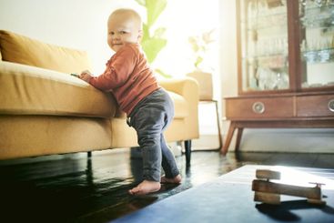 Baby boy, floor and learning to walk by couch for...