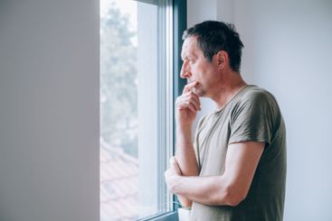 Serious caucasian male looking through window and...